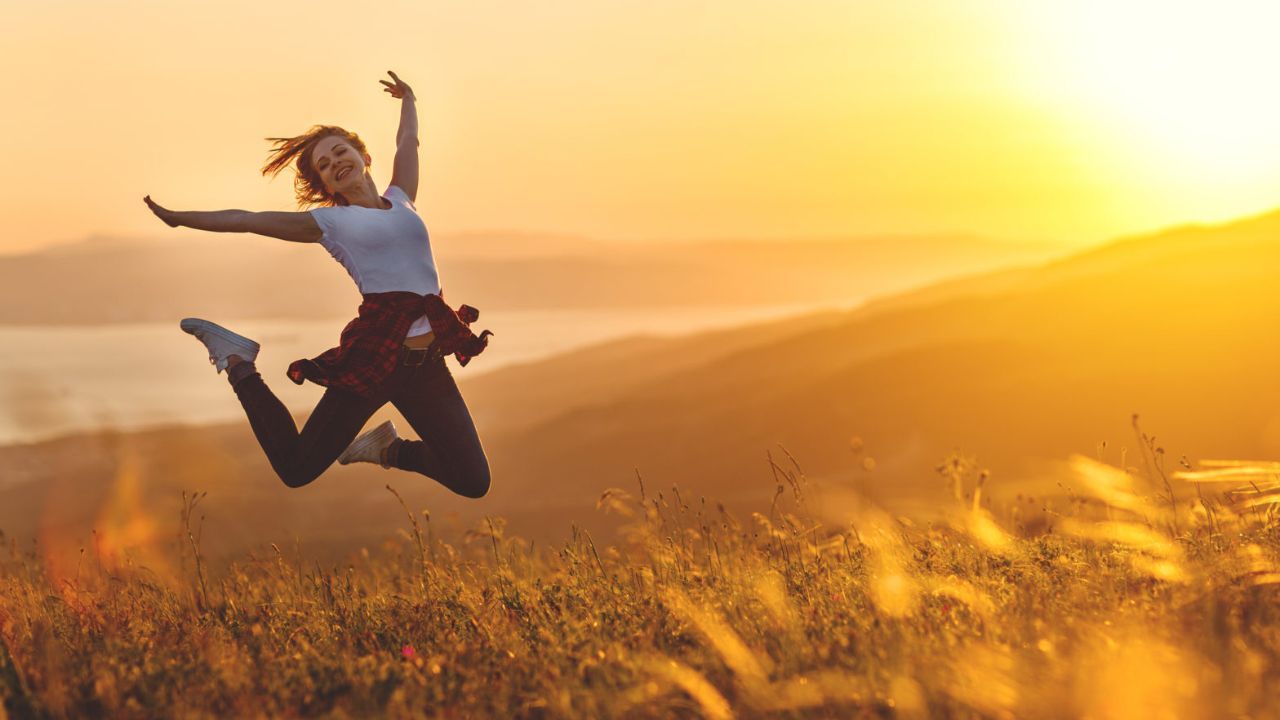 Girl Jumping high in the air in a field in the afternoon Sun 